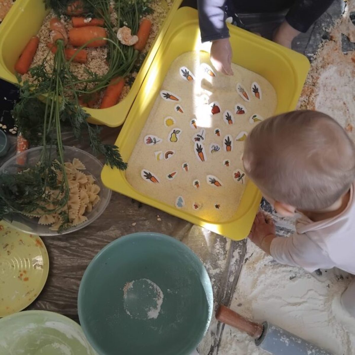 Dzieci ze żłobka bawiące się piaskiem, mąką i makaronem podczas warsztatów sensorycznych wspierających rozwój.
