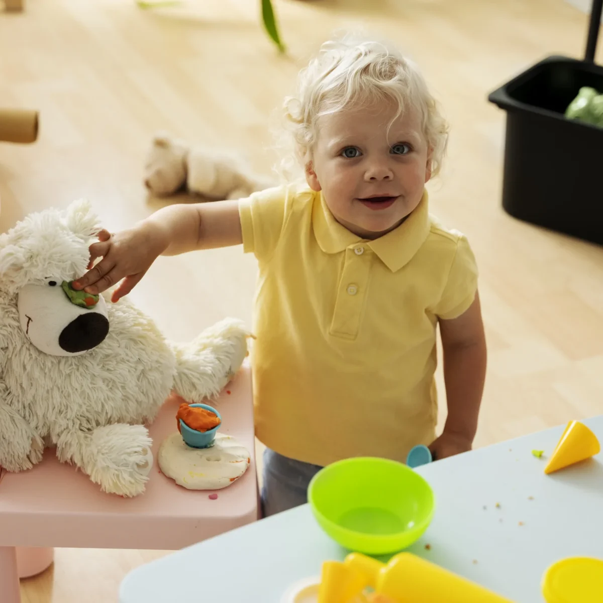 Opiekunka w żłobku przy małym dziecku, spokojnie rozmawia i wspiera je emocjonalnie podczas adaptacji w sali zabaw.